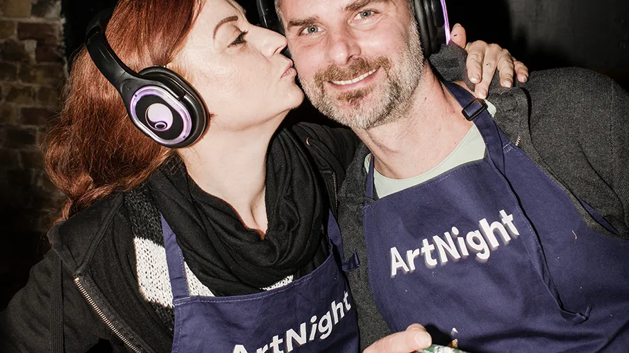 Two people wearing headphones and ArtNight aprons.