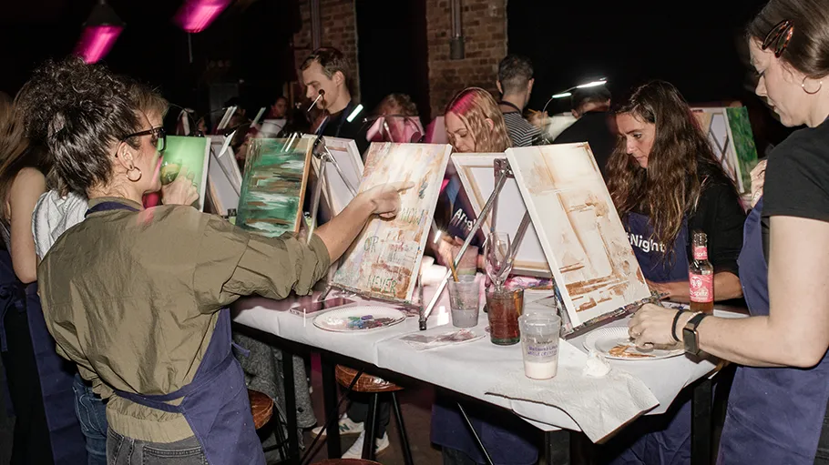 People painting canvases in a dimly lit room.