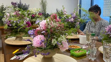 Blumengestecke auf Tisch, Person arbeitet.