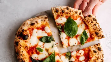 Hand nimmt ein Stück Margherita-Pizza.