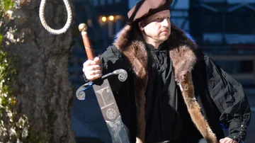 Man in period costume holding a sword outdoors.