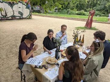 Gruppe genießt Weinprobe unter Bäumen in einem Park.
