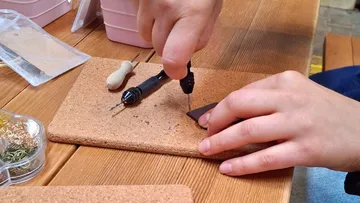 Hände basteln auf Korkbrett mit Werkzeugen.