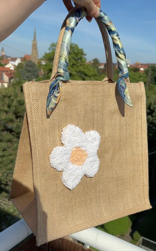 Hand hält Jutetasche mit Blumenstickerei.