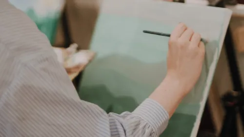 Person malt Landschaft auf Leinwand drinnen.