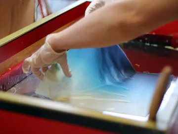 A hand draws a leaf through a colored liquid.