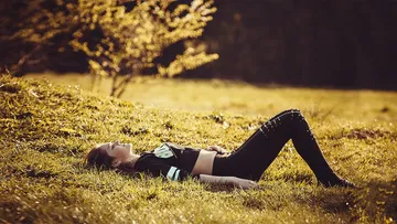Person liegt im Gras, genießt Sonnenlicht, draußen.