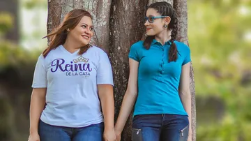 Two women standing, holding hands, near tree.