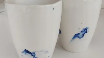 Zwei weiße Tassen mit blauen Spritzern, Nahaufnahme.