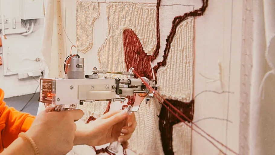 Person using tufting gun on textile artwork.