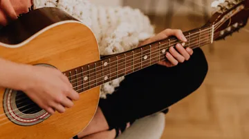 Person spielt Gitarre in gemütlichem Raum.
