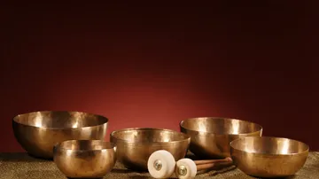 Five bronze singing bowls on a patterned cloth.