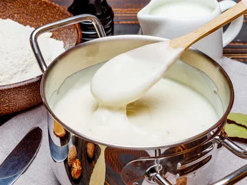 Eine Kelle schöpft cremige Sauce aus einem Topf.