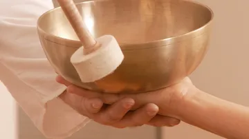Singing bowl held, wooden mallet approached.