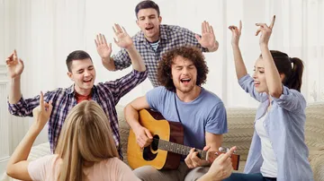 Gruppe von Freunden singt mit Gitarre drinnen.
