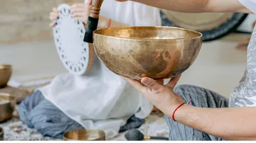 Person playing a brass singing bowl indoors.