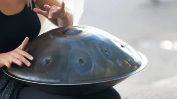 Person playing handpan drum outdoors.