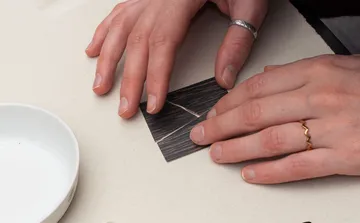 Hände falten schwarzes Papier auf Tisch.