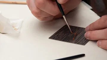 Hands painting thin wood on white surface.
