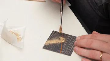 Pinsel trägt Goldpulver auf kleinen Gegenstand auf.