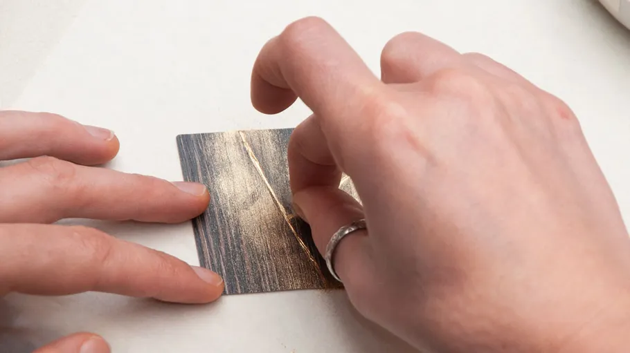 Hands applying gold leaf to black surface.