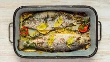 Two baked fish with lemon in roasting pan.