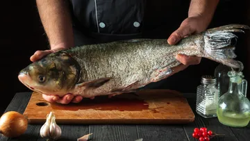 Person holding fish on wooden board.