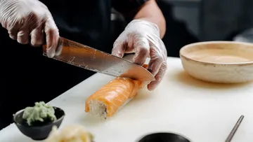 Koch schneidet Sushi-Rolle mit Messer, Küchentheke.