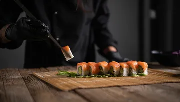 Chef placing sushi roll on wooden table.