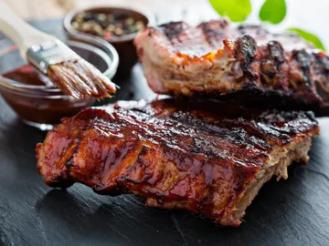 Grilled ribs are coated with sauce on a plate.