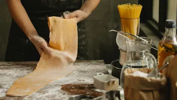 Person rolling pasta dough on floured surface.