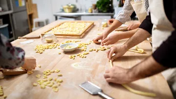 People making pasta on wooden table.