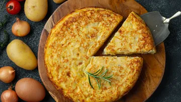 Tortilla on wooden board with ingredients nearby.
