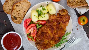 Schnitzel with potatoes, tomato salad, bread, and ketchup.