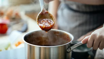 Person schöpft Tomatensauce aus Topf.