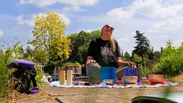 Woman seated, playing singing bowls outdoors.