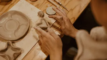 Person shaping clay on a wooden table.