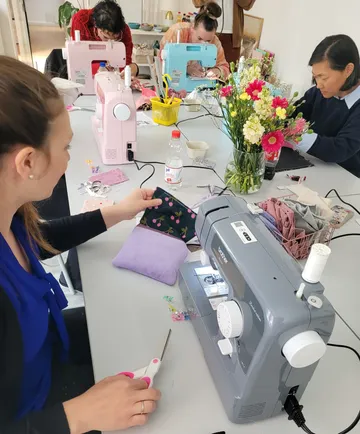 Women sewing with machines at shared table.