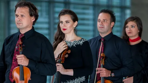 Four musicians hold violins indoors.