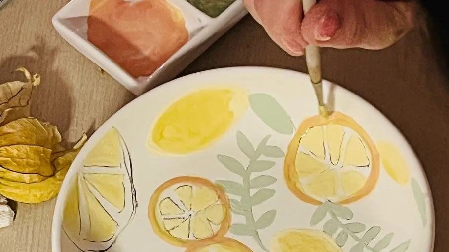 Person painting citrus designs on a plate.