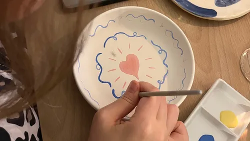 Person painting pink heart on ceramic plate.