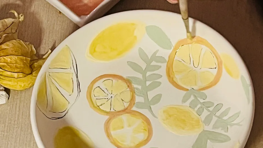 Person paints lemon design on a plate.