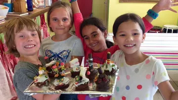 Children holding a tray of decorated cakes.