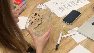 Person hält Glas mit 'Home Sweet Home' Text.