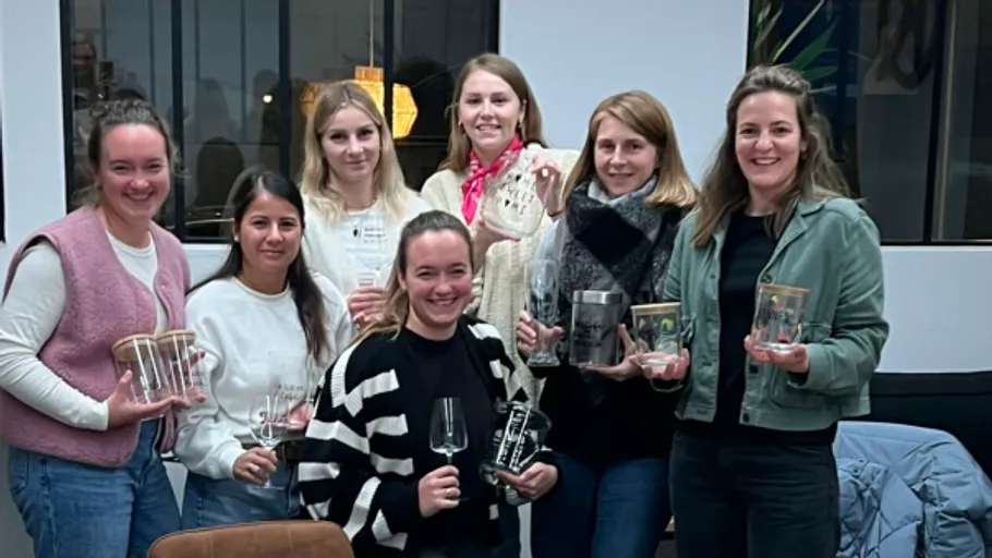 Seven women smiling, holding awards in an office.