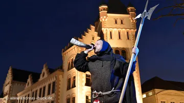 Mann in mittelalterlicher Kleidung bläst Horn, Schloss dahinter.