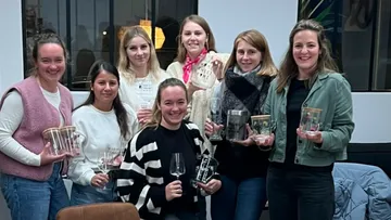 Sieben Frauen lächeln, halten Glastrophäen drinnen.