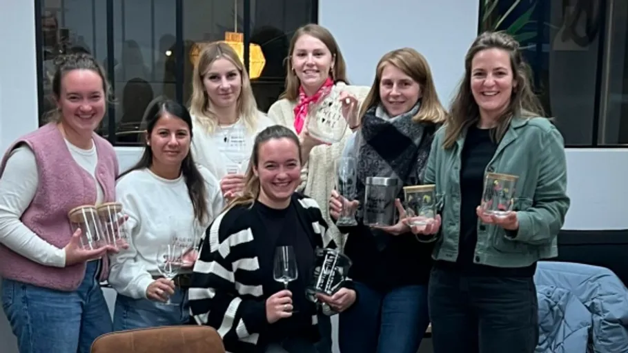 Seven women smiling, holding glass trophies indoors.