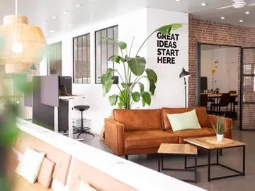 Büro mit Sofa, Pflanze, Motivationsspruch und Tischen.
