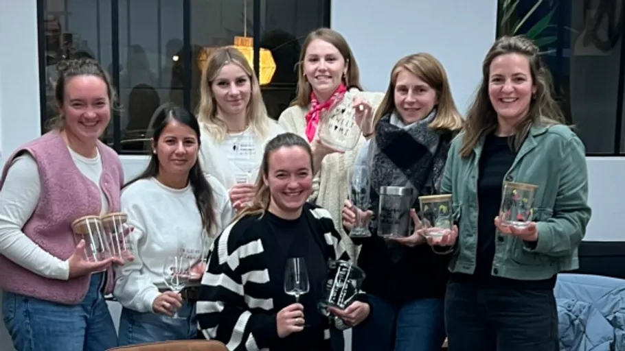 Seven women holding glassware indoors, smiling together.